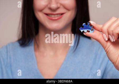 Place for text. A smile of a girl holding a wooden blue puzzle in her hand. Advertising photo of unique puzzles. Stock Photo