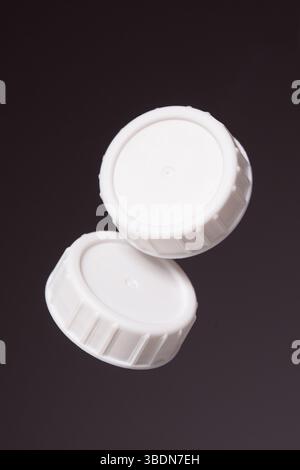 Two white plastic bottle caps on a black background. Close up. Stock Photo