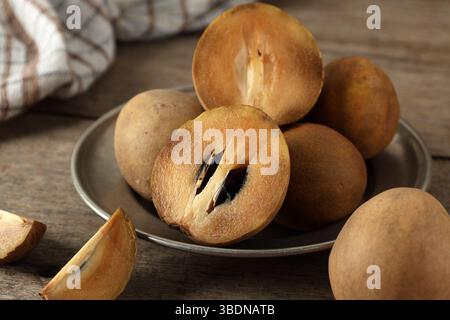 Manilkara zapota or Sawo  Fruit or commonly known as Sapodilla, Sapota, Chikoo, Chico, Naseberry, or Nispero. Half Buah SAwo on Silver Plate Above Woo Stock Photo
