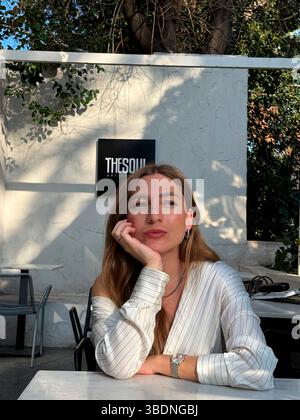 Young woman enjoys a moment of reflection at a stylish cafe in a sunny outdoor setting Stock Photo