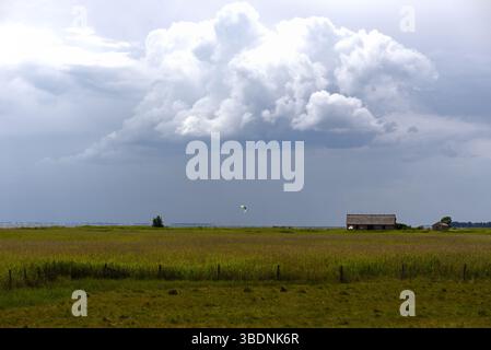 Dramatic thunderclouds over a North German meadow landscape with barn and kitesurfer Stock Photo
