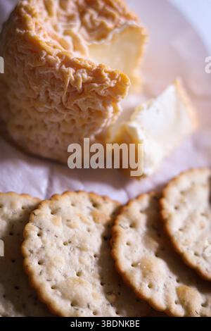French Langres cheese with a wrinkled washed rind and ripe interior, seeved with herb crackers and home made chutney on a wooden bamboo board Stock Photo