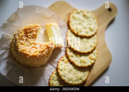 French Langres cheese with a wrinkled washed rind and ripe interior, seeved with herb crackers and home made chutney on a wooden bamboo board Stock Photo