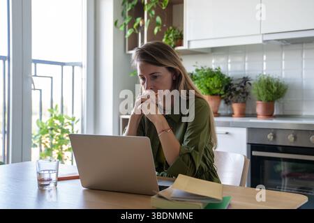 Focused thoughtful woman with laptop deep in process of solving tasks problems remote work IT field. Stock Photo