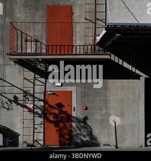 Lublin, Poland, 21 May 2025 red balcony doors against grey wall of a building with contrasting shadows Stock Photo