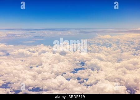 White fluffy clouds viewed from airplane at high altitude with clear blue sky above the horizon. Stock Photo