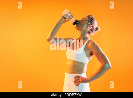 Beautiful mature sportive woman wearing sportswear doing workout - fit, mature woman in sportswear drinking water after an intense workout, glistening Stock Photo