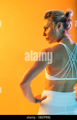 Beautiful mature sportive woman wearing sportswear doing workout - muscular mature woman in white sportswear posing with hands on hips and looking ove Stock Photo