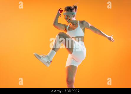 Beautiful mature sportive woman wearing sportswear doing workout - fit senior woman in white sportswear and headband performing dynamic exercises on a Stock Photo