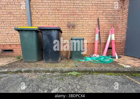 Photograph of local council rubbish bins and other discarded items located in the carpark near a brick wall at the rear of a large building. Stock Photo