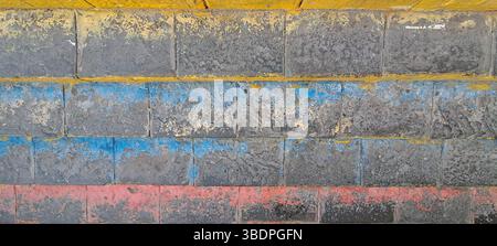 Old brick wall featuring faded red, blue, and yellow paint layers Stock Photo