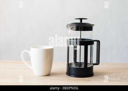 Coffee Cup and French Press on Wooden Table with Light Background Stock Photo