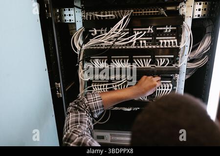Technician managing network cables in a server room during the afternoon hours Stock Photo