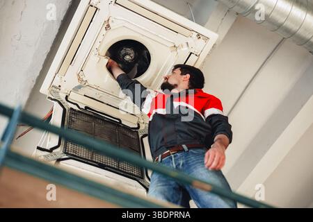 Technician performs maintenance on air conditioning unit in commercial building during daylight hours Stock Photo
