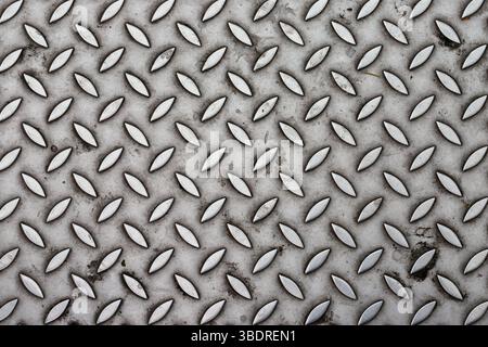 Close-up shot of a textured metal surface. The pattern consists of raised, elongated oval shapes arranged diagonally. The color is primarily gray. Stock Photo