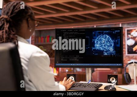 Teleworking system administrator using computer for artificial intelligence computing through self learning algorithms. African american remote worker works with AI deep neural networks on desktop PC Stock Photo
