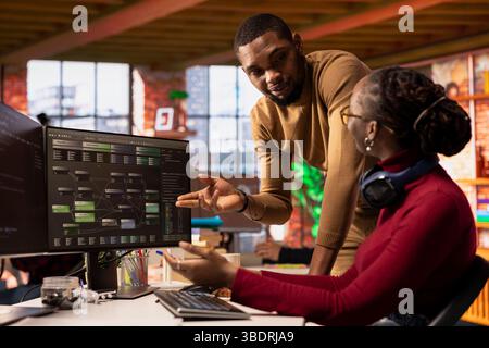 IT startup office coworkers doing brainstorming, designing and implementing algorithms enabling machine learning. Team of tech venture employees collaborating to review code and fix bugs Stock Photo