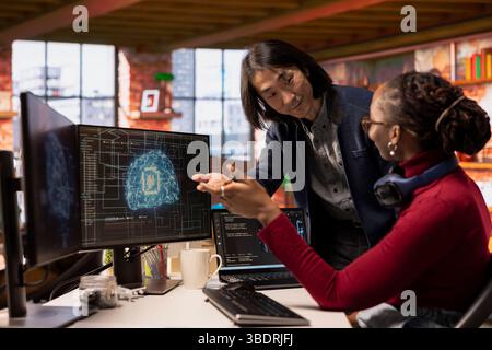 CTO manager in multiethnic startup office helps technician coding advanced AI algorithm and machine learning models. Team leader overseeing work done by employee in Silicon Valley workplace Stock Photo