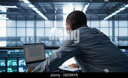 Technician coding on laptop in data center, managing server virtualization, finetuning network protocols. Server farm employee programming on notebook, enforcing advanced security measures, camera B Stock Photo