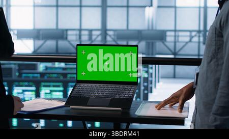 Coworkers in data center using mockup laptop, integrating green technologies. IT experts in server room using chroma key notebook to implement sustainable energy solutions, camera A close up Stock Photo