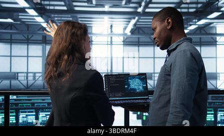 Software developers using AI tech on laptop in data center managing server virtualization. IT expert coding on notebook in server room using artificial intelligence, finetuning network, camera B Stock Photo