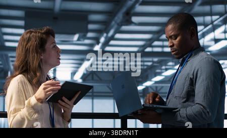 Colleagues in data center workplace use laptop to calibrate energy usage. Server farm IT specialist using notebook to inspect UPS configurations, doing maintenance on equipment, camera A Stock Photo