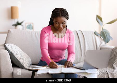 Planning Trip. Happy black woman choosing travel destination on map at home Stock Photo