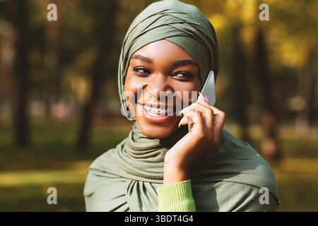 Cheerful African American Muslim Female Talking On Cellphone Standing Outdoors Stock Photo
