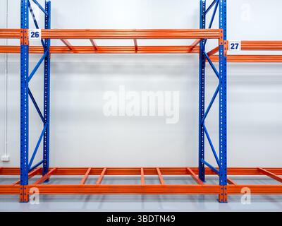 Empty red and blue metal warehouse rack, steel shelves with number panels sign, installed on bright white clean factory wall background. Product stora Stock Photo