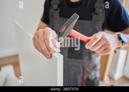 Close up of hammer hitting nail. Man in work clothes using hammer to assemble furniture detail. DIY home improvement concept Stock Photo