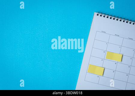 Calendar page with yellow adhesive notes. On top of blue surface, high angle view. Copy space. Stock Photo