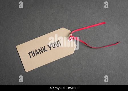 Thank you tag with red ribbon, on top of dark surface. Top view. Stock Photo