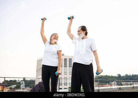 Happy senior couple exercising outdoors using light dumbbells on sunny day Stock Photo