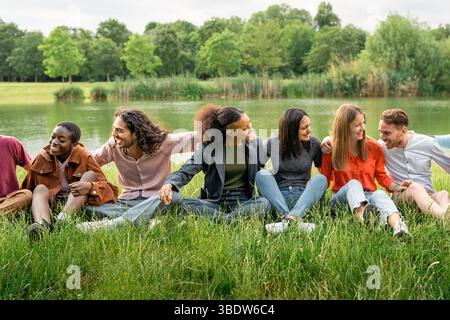 Multicultural group of young students sitting on the grass, building unity and sharing an authentic moment of connection and inclusion outdoors. Stock Photo