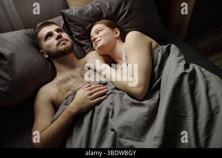 Caucasian couple lying in bed sharing a tender and intimate moment. Woman resting her head on man's chest, both looking relaxed and content Stock Photo