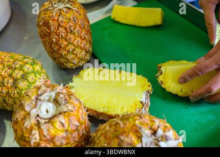 hands preparing fresh pineapple on green cutting board in kitchen Stock Photo
