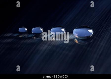 Four round water droplets on a dark blue, textured surface. V3 Stock Photo