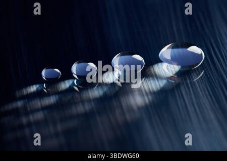 Four round water droplets on a dark blue, textured surface. V2 Stock Photo