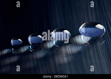 Four round water droplets on a dark blue, textured surface. Stock Photo