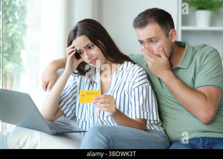 Worried couple having trouble paying online with credit card and laptop sitting on a couch at home Stock Photo