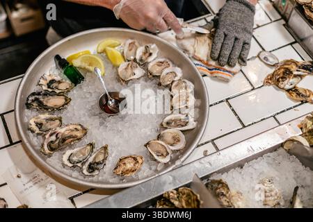 Fresh oysters being shucked and served on ice with lemon wedges Stock Photo