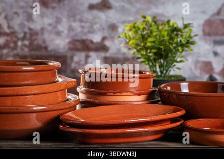 Rustic clay plates and bowls stacked on a wooden table, against a rustic white wall. Stock Photo