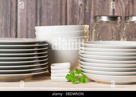 White tableware with plates and bowls next to some glass jars, on a light wooden background. Stock Photo