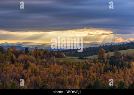 Sun rays shining through clouds over colorful autumn forest landscape with Low Tatras Stock Photo
