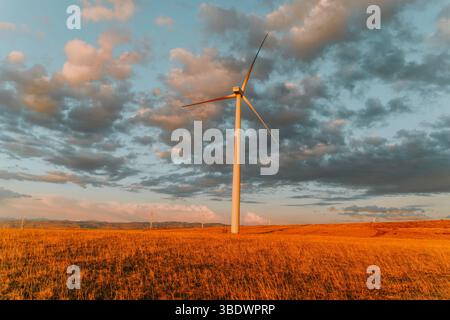 Single wind turbine stands tall against moody evening sky. Stock Photo