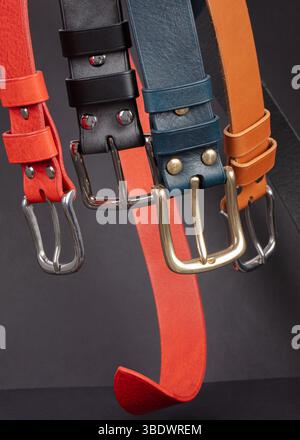 Various leather belts with metal buckles close-up on dark grey background. Stock Photo