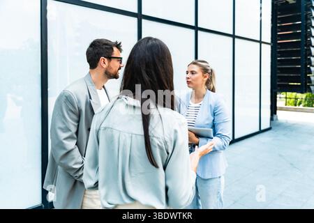 Diverse business team of corporate professionals in formal attire collaborating outdoors, engaged in strategic discussion while analyzing data on lapt Stock Photo