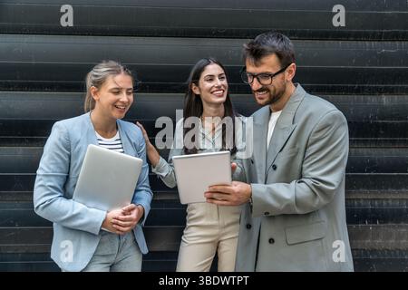 Diverse business team of corporate professionals in formal attire collaborating outdoors, engaged in strategic discussion while analyzing data on lapt Stock Photo