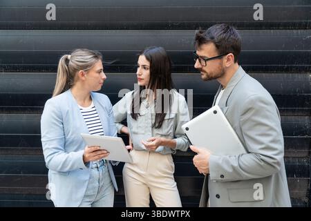 Diverse business team of corporate professionals in formal attire collaborating outdoors, engaged in strategic discussion while analyzing data on lapt Stock Photo