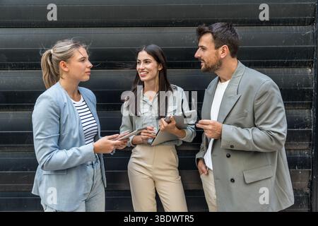 Diverse business team of corporate professionals in formal attire collaborating outdoors, engaged in strategic discussion while analyzing data on lapt Stock Photo